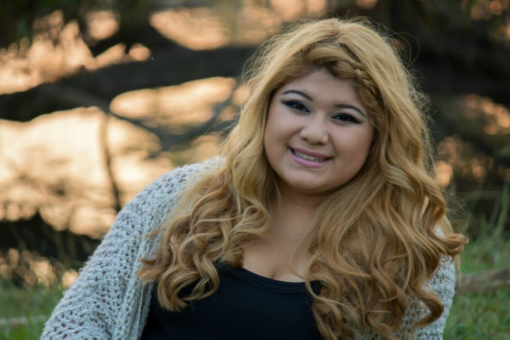 A young woman poses for a senior photo while sitting outdoors by a lake.