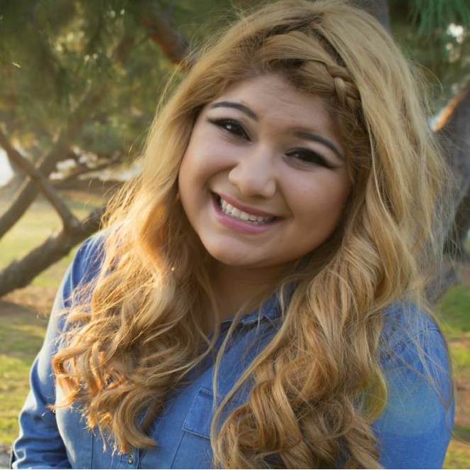 A young woman poses for a senior photo while sitting outdoors in a park.