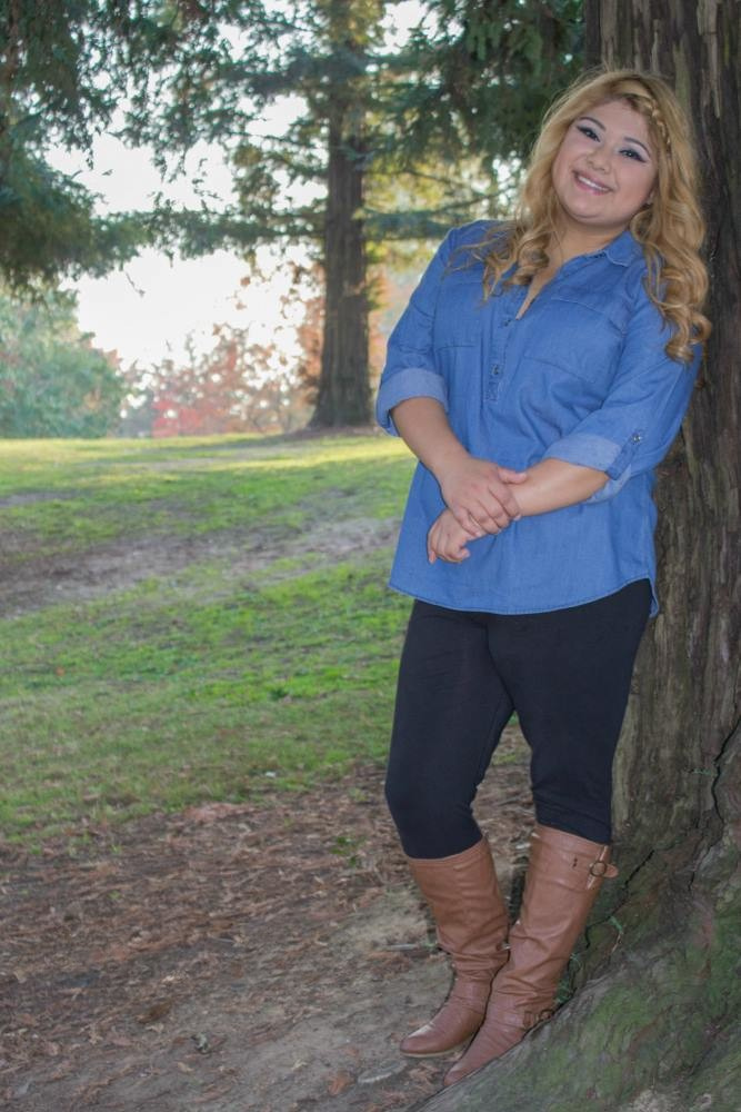 A young woman poses for a senior photo while standing near a tree in a park.