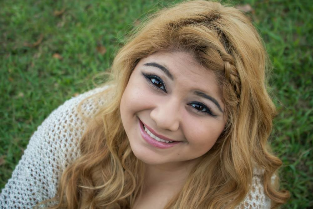 A young woman poses for a senior photo while sitting in the grass.