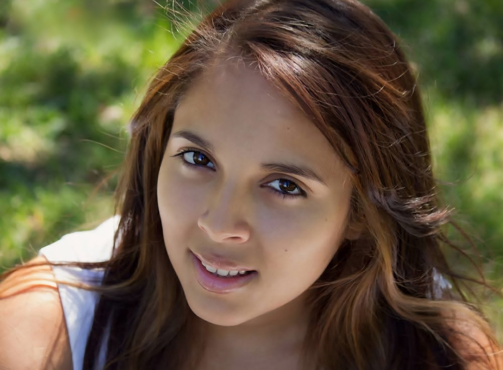 A young woman poses for a senior photo while sitting in the grass.