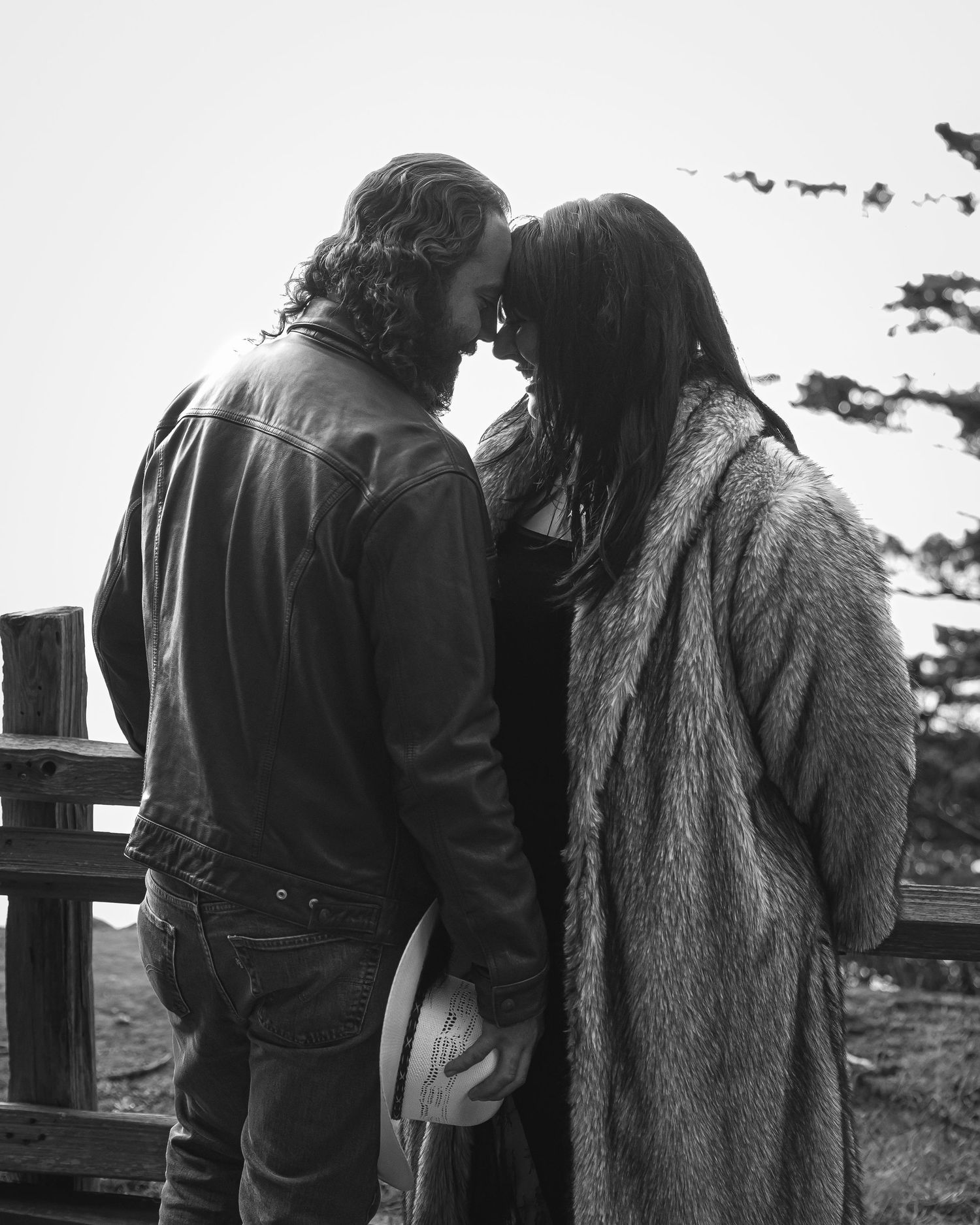 A joyful couple embraces and laughs together in a garden with palm plants in the background.