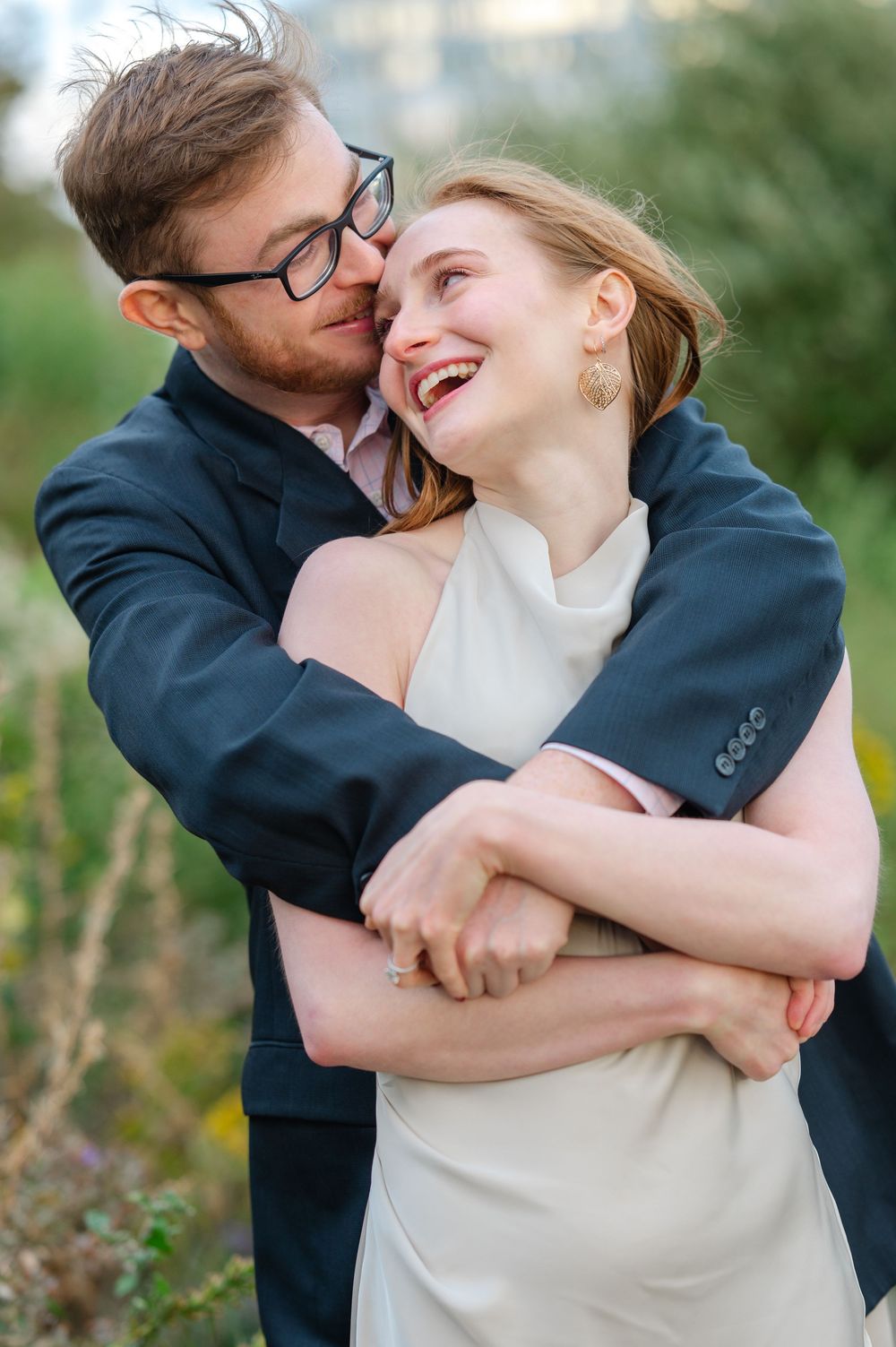 Man embracing woman from behind as she laughs joyfully outdoors in natural light.