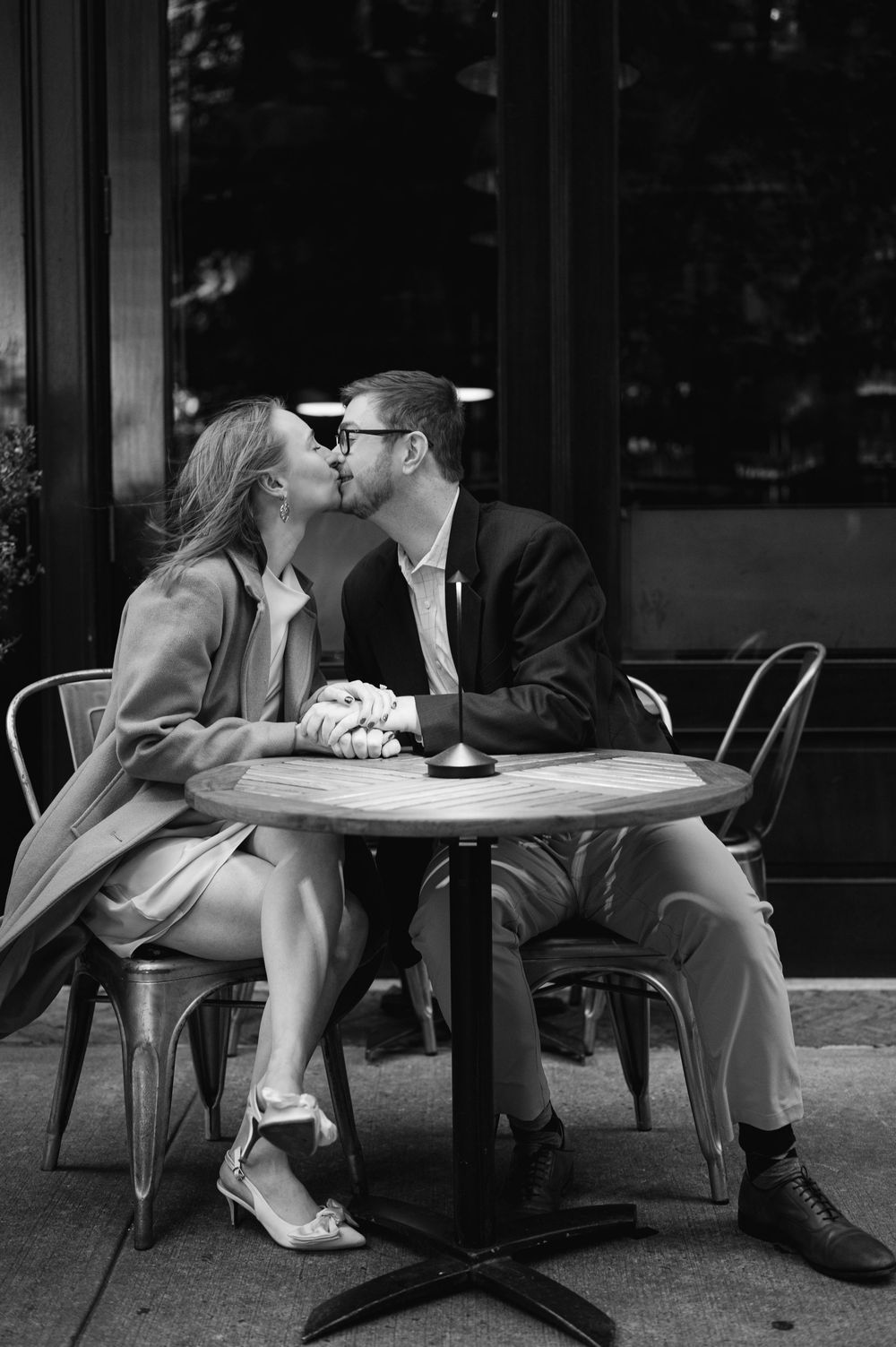 Couple sharing a tender kiss at an outdoor cafe table in a romantic black and white portrait.