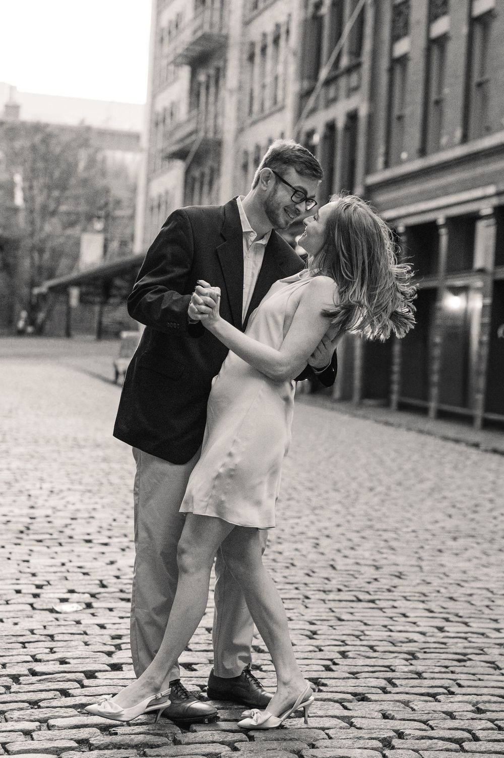 A couple dances together on a cobblestone street, gazing into each other's eyes in the city.