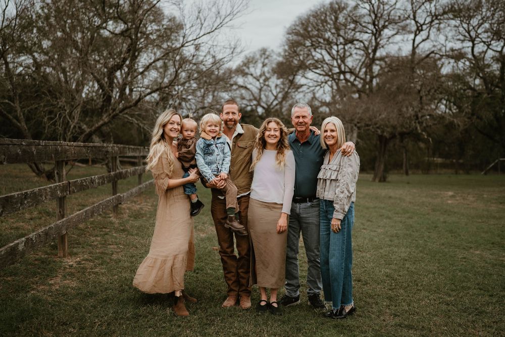 Happy multigenerational family smiling together outdoors near a wooden fence on a green lawn.