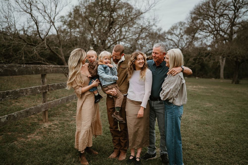 A joyful multigenerational family poses together outdoors on a green lawn near a wooden fence.