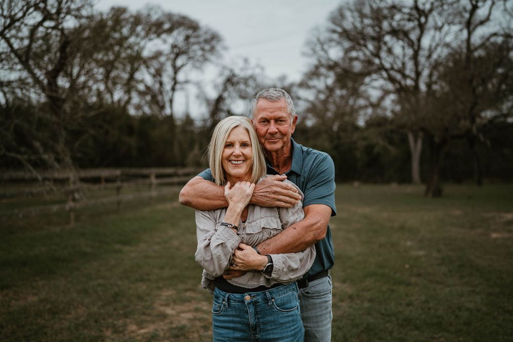 Smiling older couple embracing outdoors in a green park setting with trees in the background.