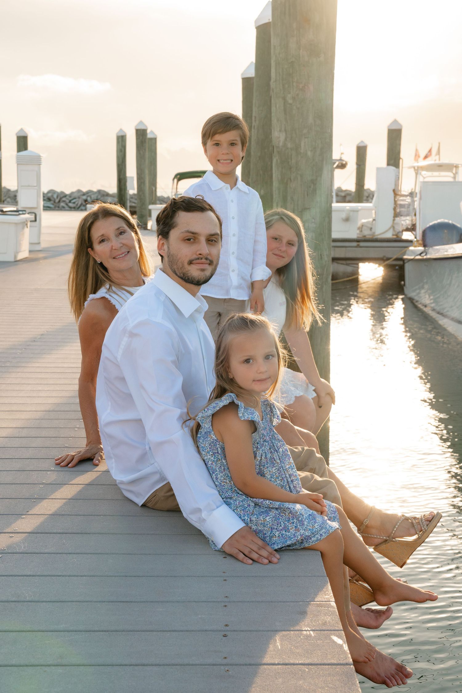 Family of five sitting on marina dock at golden sunset with boats in background.