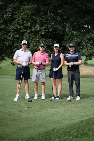 Four golfers posing together on a lush golf course, smiling and holding clubs on a sunny day.