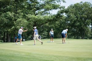 Golfers on a lush green golf course surrounded by tall trees on a sunny day.