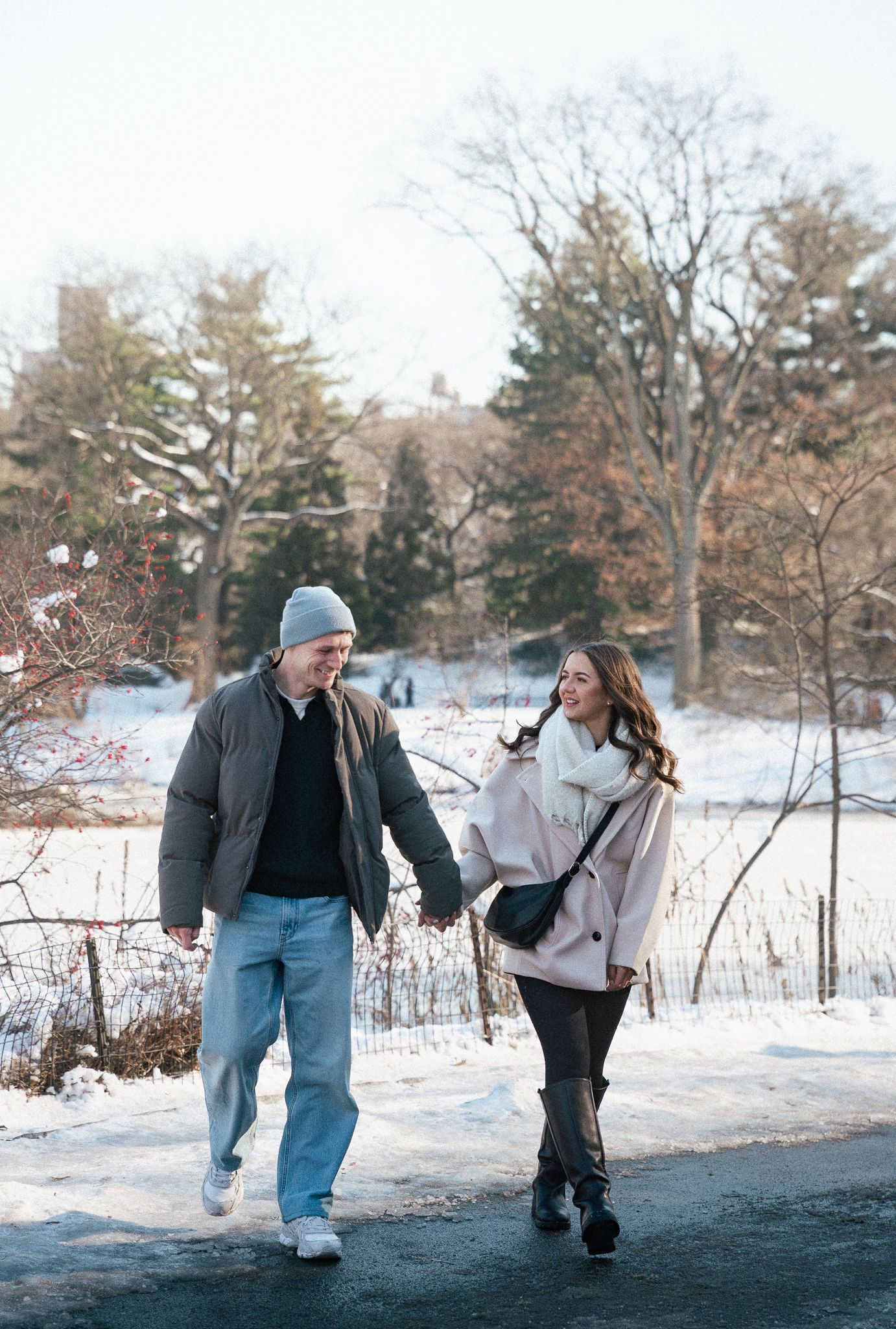 Couple holding hands and walking on a snowy path in Central Park during winter.