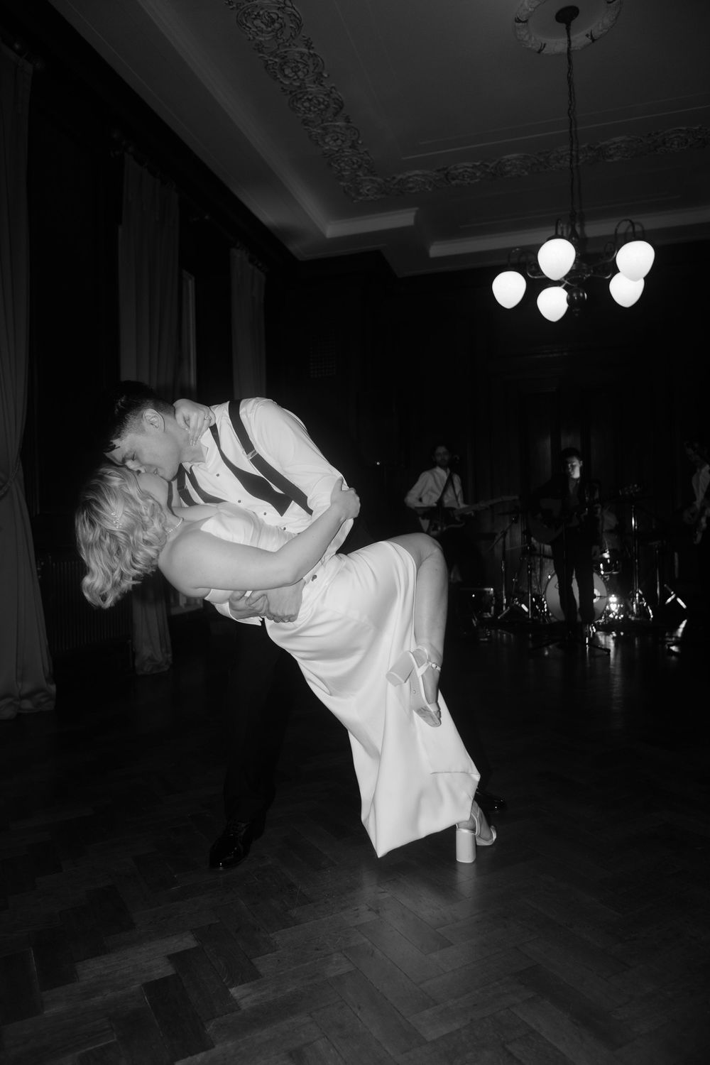 Black and white photo of a couple sharing a romantic dip kiss on the dance floor at a wedding reception.