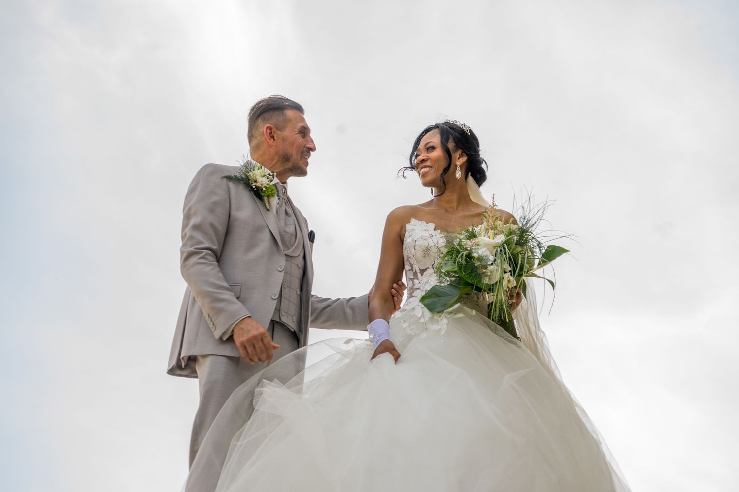 Romantic wedding couple embracing on a cobblestone street in autumn, bride wearing a white gown and pink scarf.