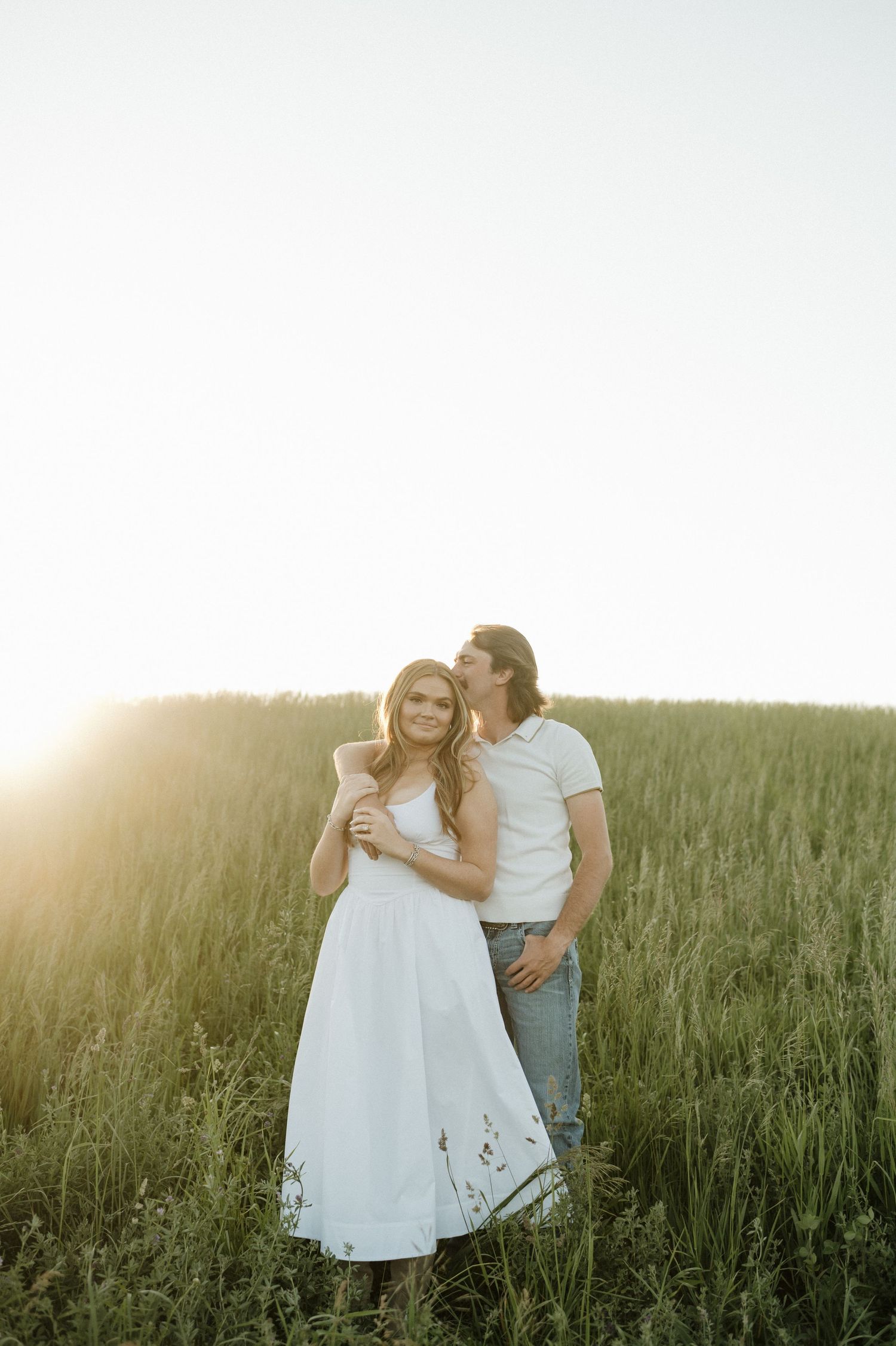 Smiling couple in green field at sunset holds their infant daughter dressed in pink between them.