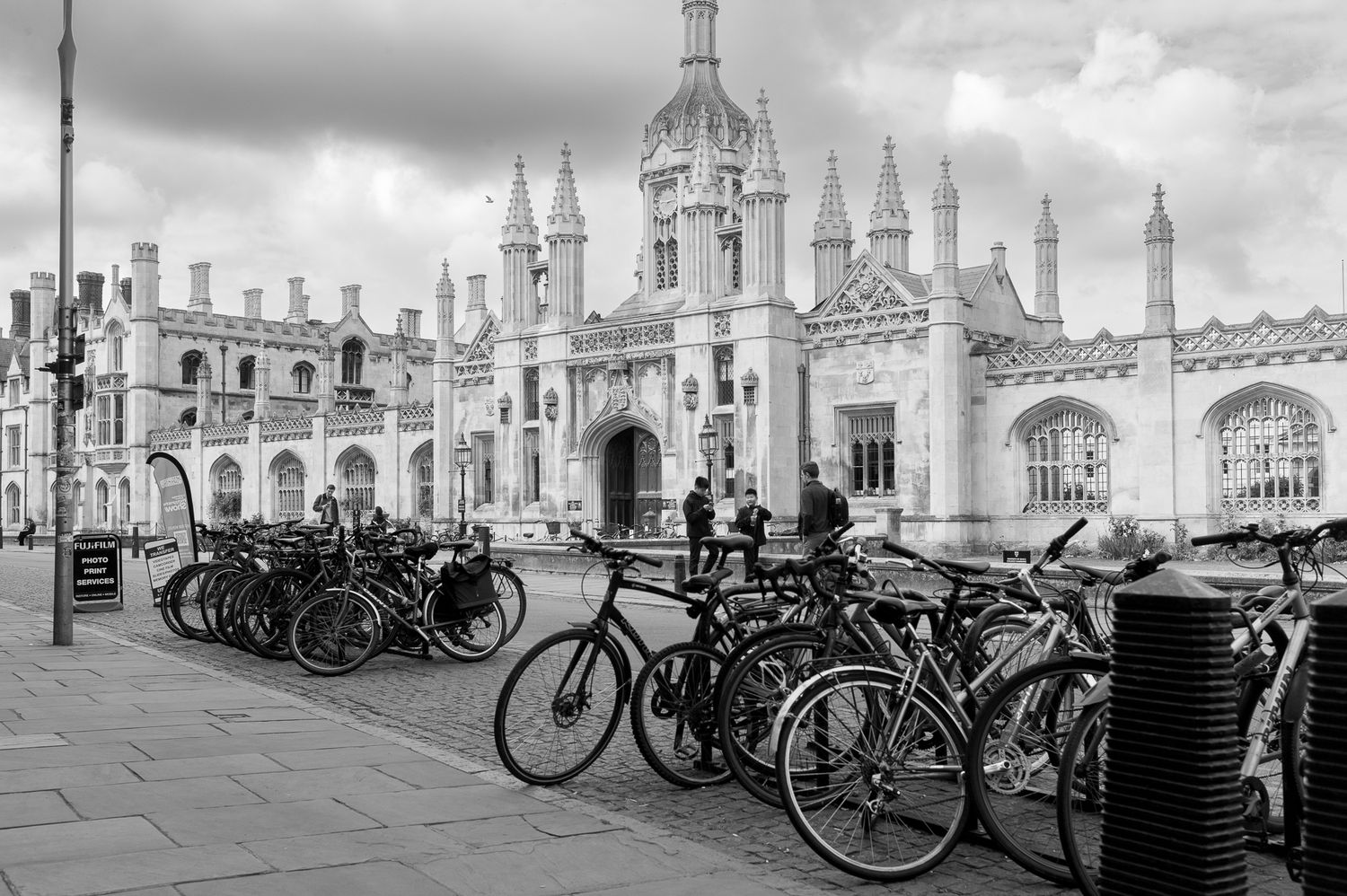 Black and white photo of bicycles parked outside ornate Gothic architecture of Kings College Cambridge.