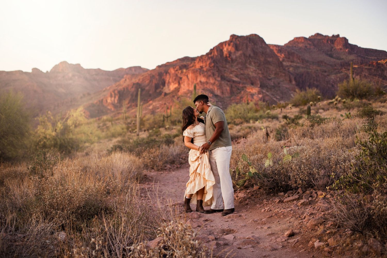 Couple sharing a romantic kiss at golden hour in the Arizona desert with red rock mountains in the background.