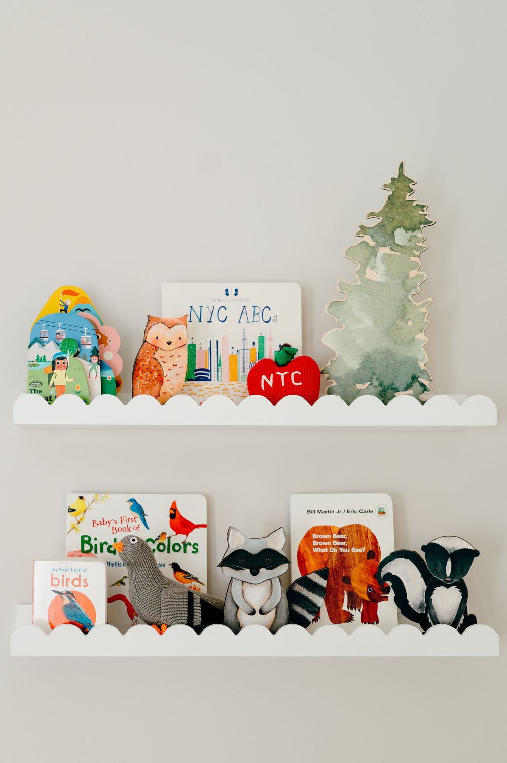 White floating shelves with woodland animal toys, NYC-themed books, and colorful children's picture books.