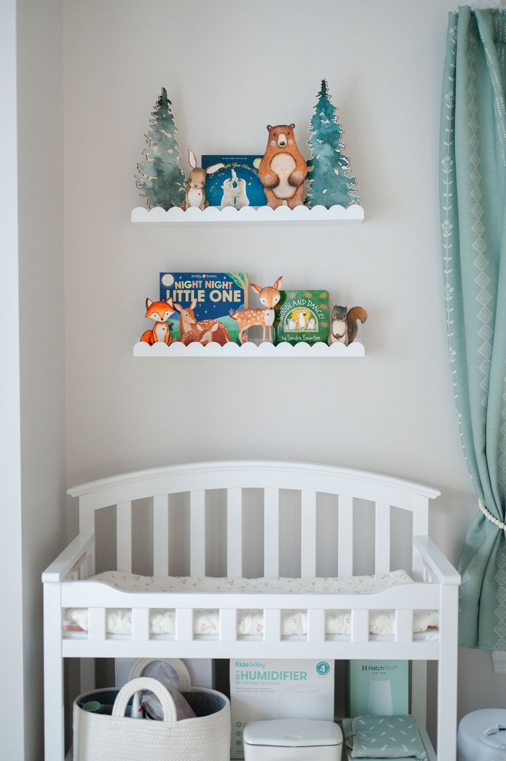 White nursery crib with woodland animal themed shelves displaying books and decorative figurines above.