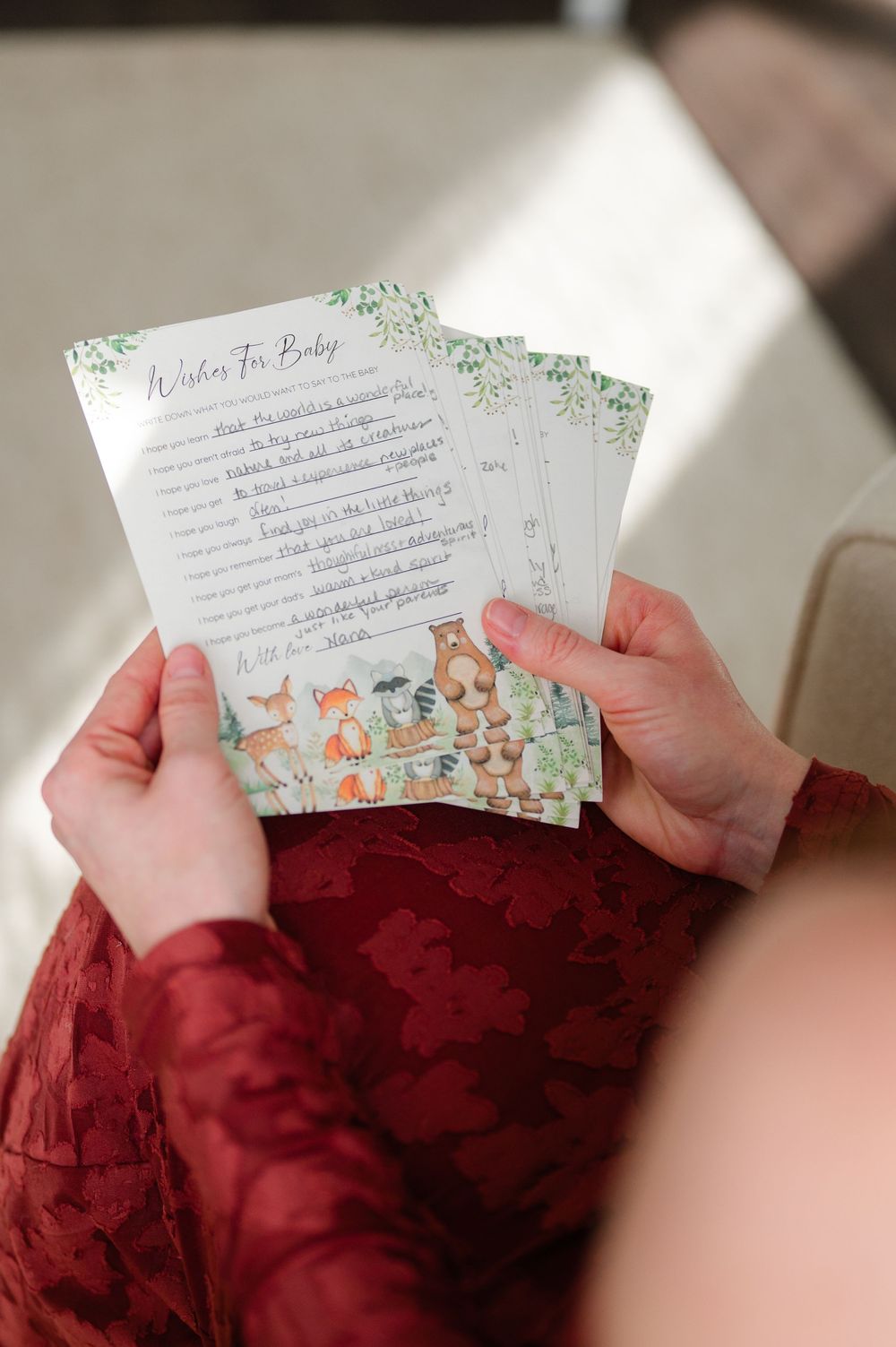 Pregnant woman holding woodland animal themed Wishes For Baby shower cards on her lap.
