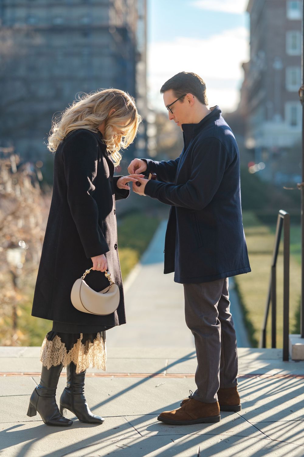 Couple sharing a romantic marriage proposal moment outdoors on a sunny day, man placing ring on womans finger.