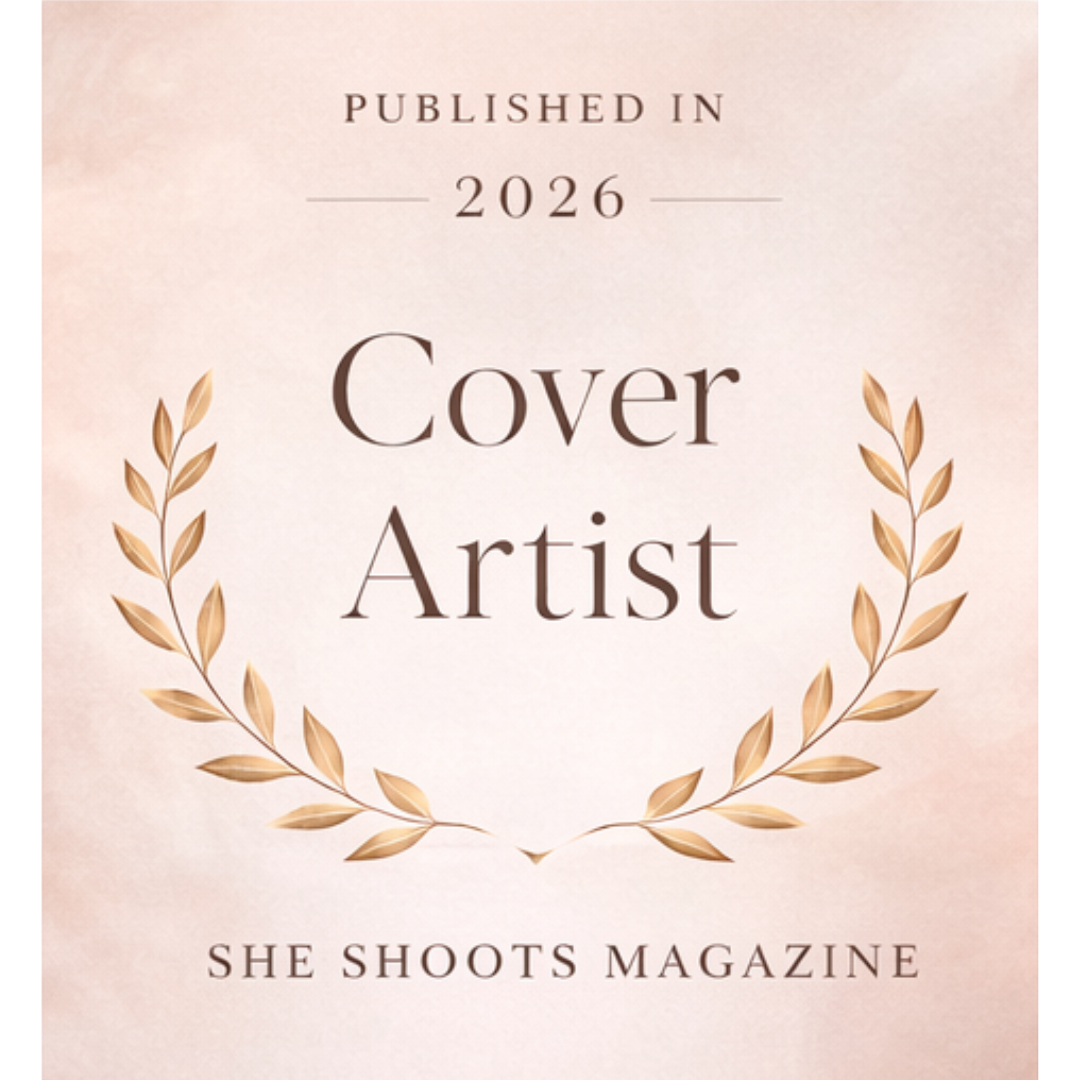 She Shoots Magazine 2026 Cover Artist publication badge with gold laurel wreath on pink background.