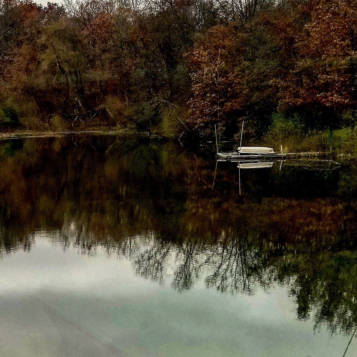 Flat bottom boat docked on still lake with autumn tree reflections Northern Missouri