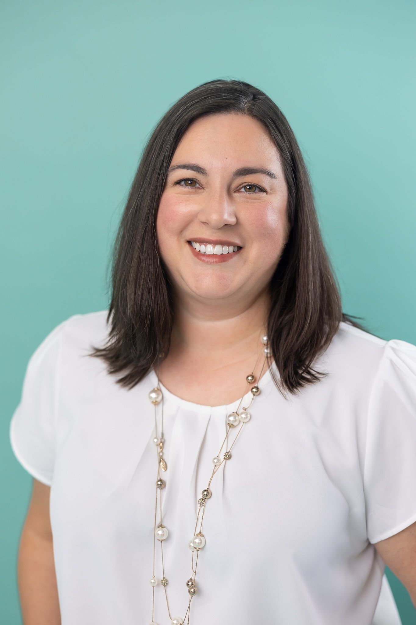 woman business book keeper for small businesses in Bellevue, WA headshot wearing white blouse and long necklace on brand teal background