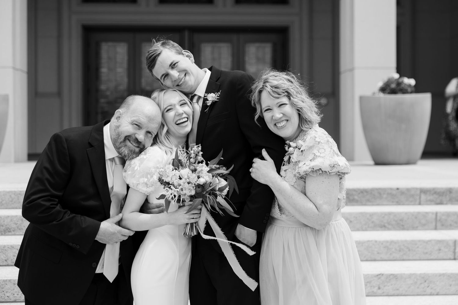 Bride and Groom smiling with their parents utilizing Family Photo List on their Wedding Day
