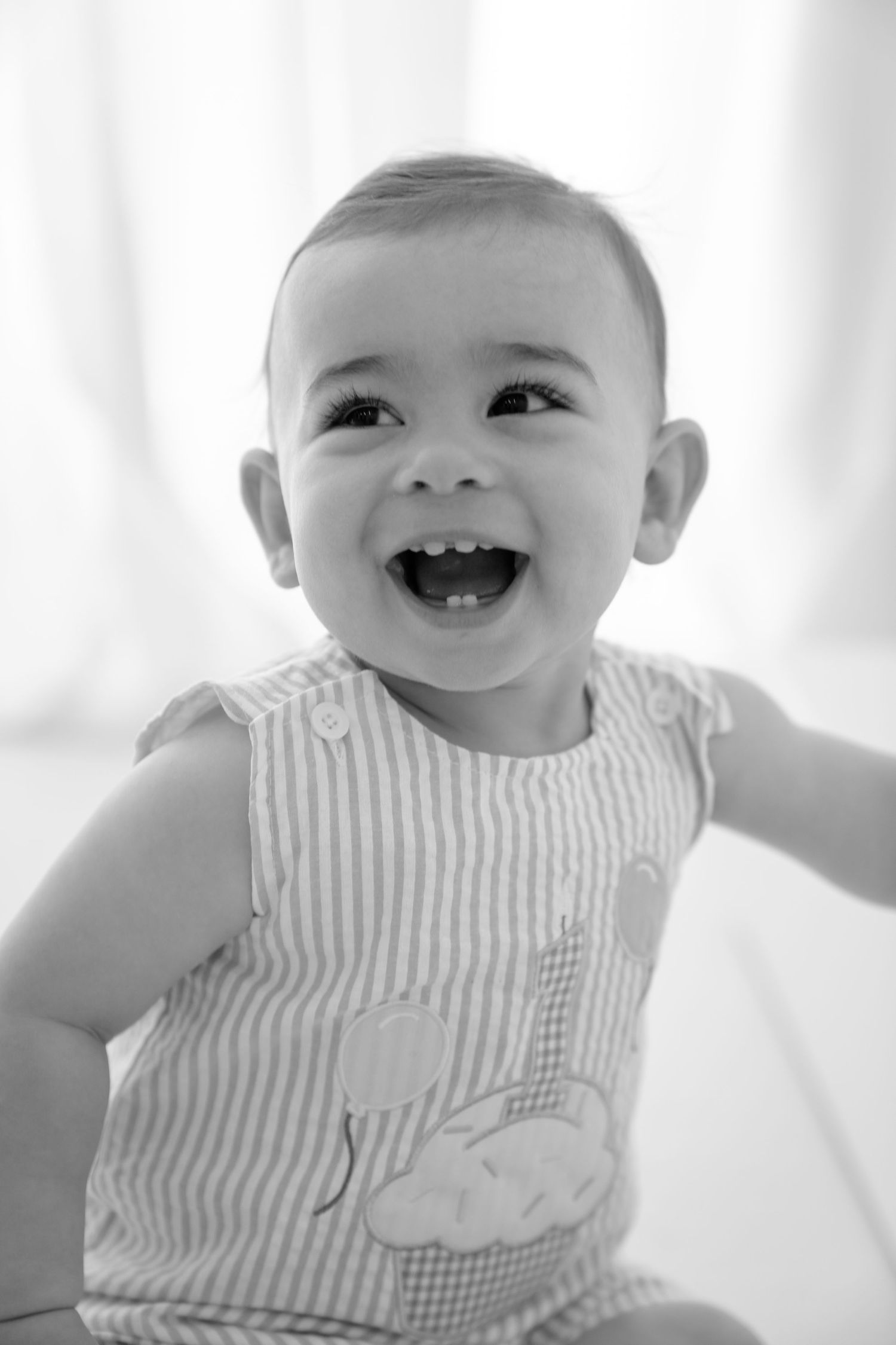 Black and white photo of a happy laughing baby in a striped romper with cupcake applique.