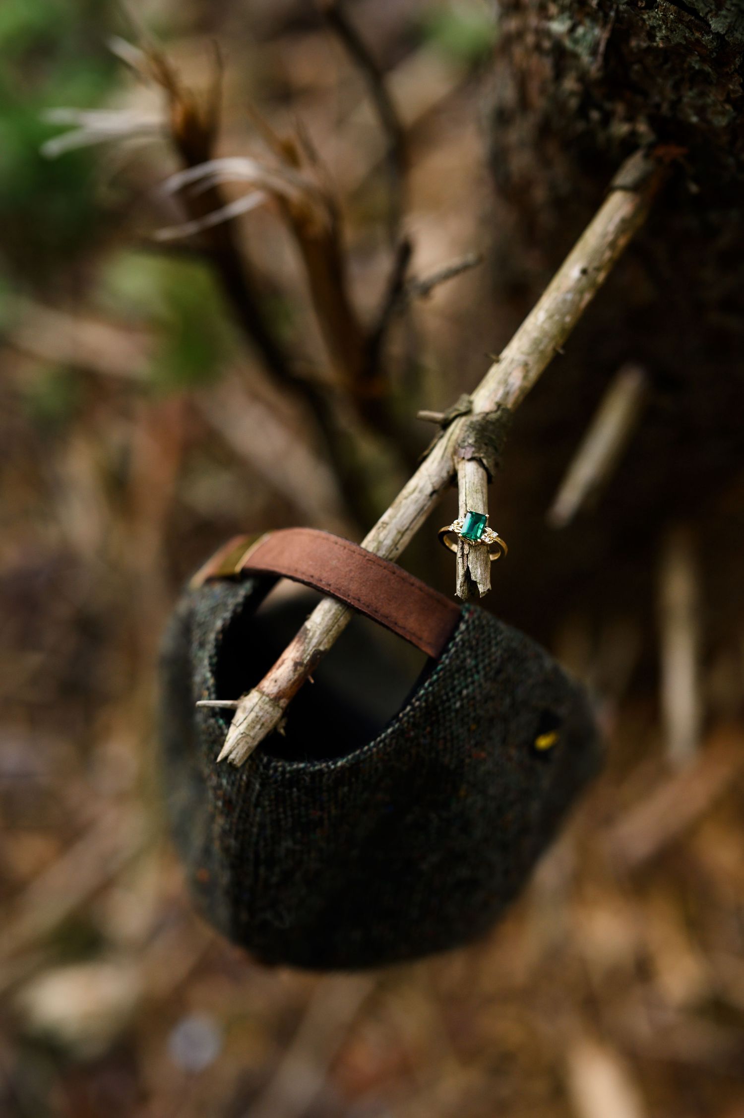A dark wool pouch hanging from a tree branch with a decorative ring resting on the branch in a forest setting.