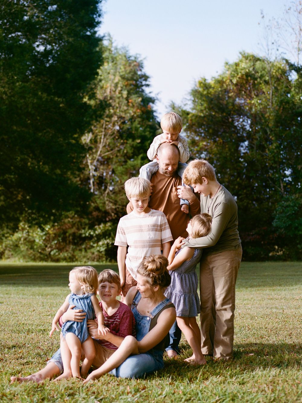 Large family with children posing together on green lawn surrounded by trees on a sunny day.