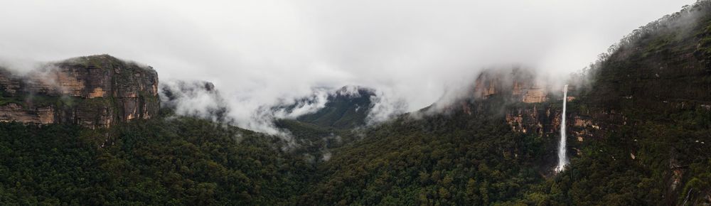Panoramic view of a lush green valley with a tall waterfall cascading down misty cloud-covered mountains in Peru.