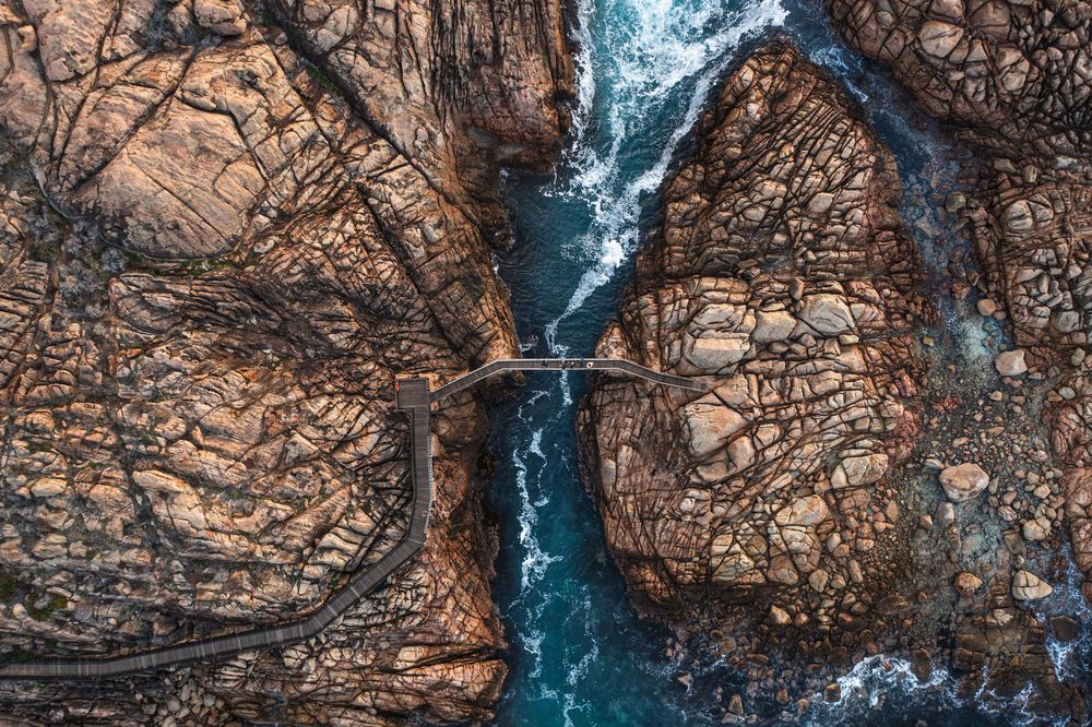 Aerial view of a narrow river gorge with a small bridge between rugged rocky cliffs and flowing turquoise water.