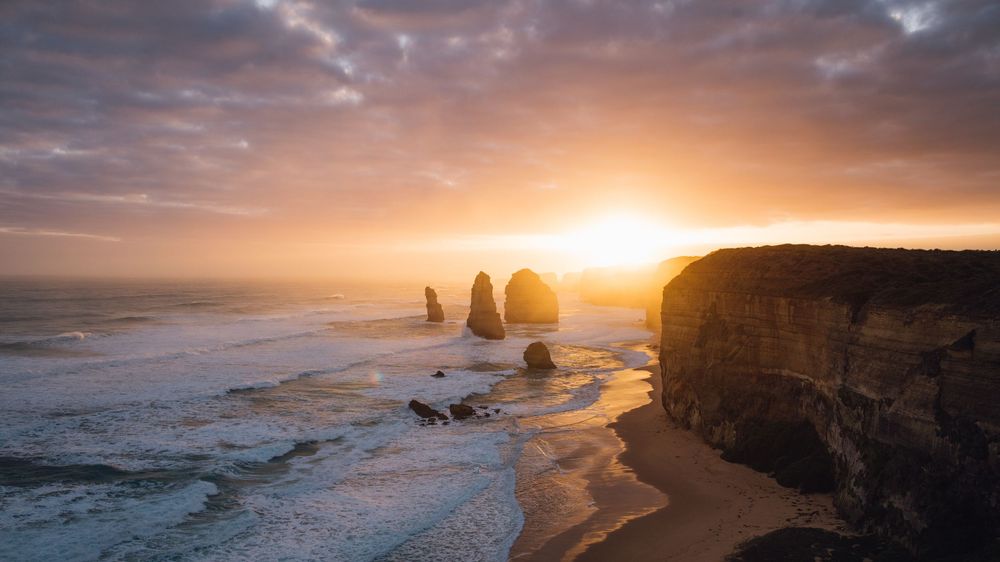 Dramatic sunset over the Twelve Apostles rock formations along Australia's Great Ocean Road with golden light.