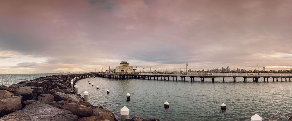 Panoramic view of a historic pier extending into calm ocean waters under a dramatic cloudy sky at dusk.