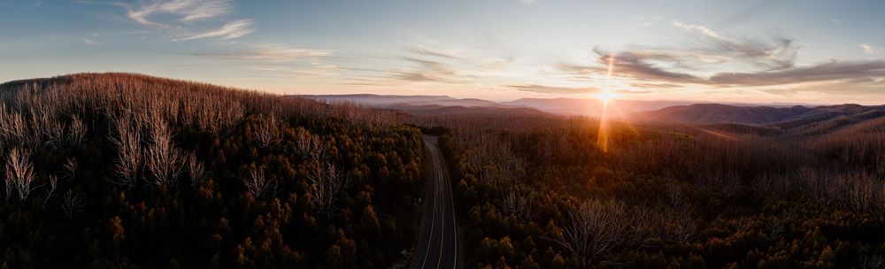 Aerial panoramic view of a winding road through autumn forest at sunset with mountain ridges in the background.