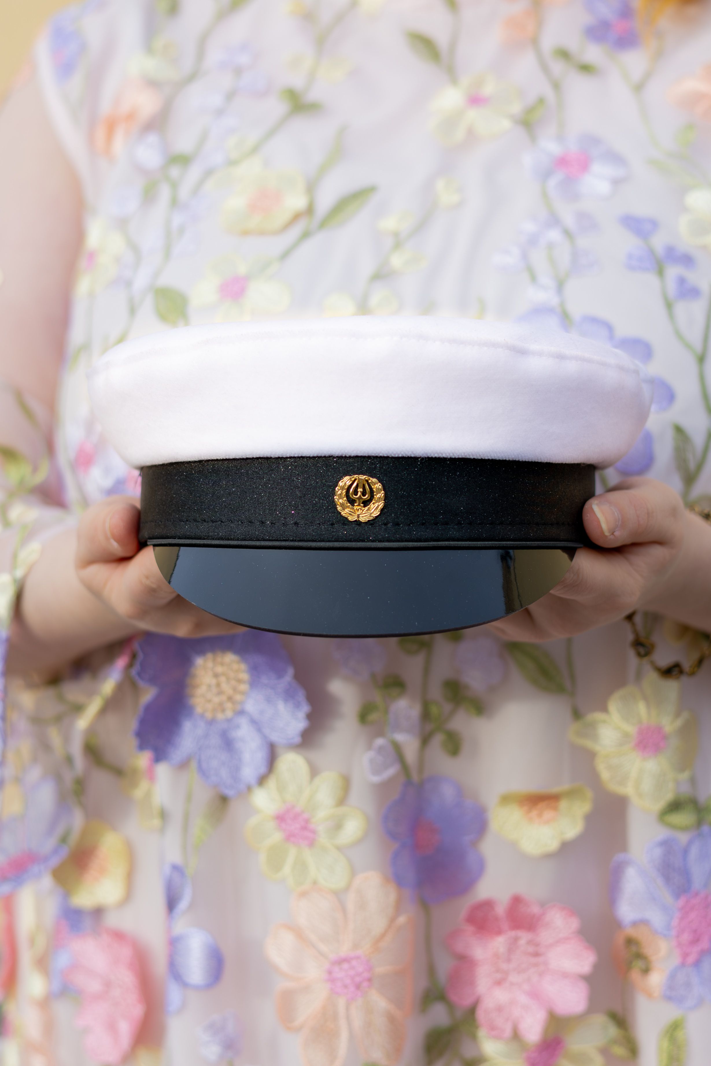 Person in floral dress holding a white and navy captain's hat with gold emblem.