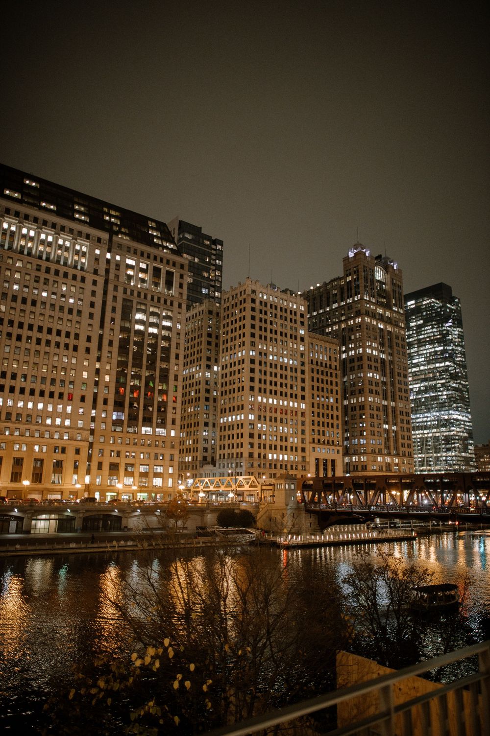 Chicago skyline at night with illuminated skyscrapers reflecting golden light on the river below.