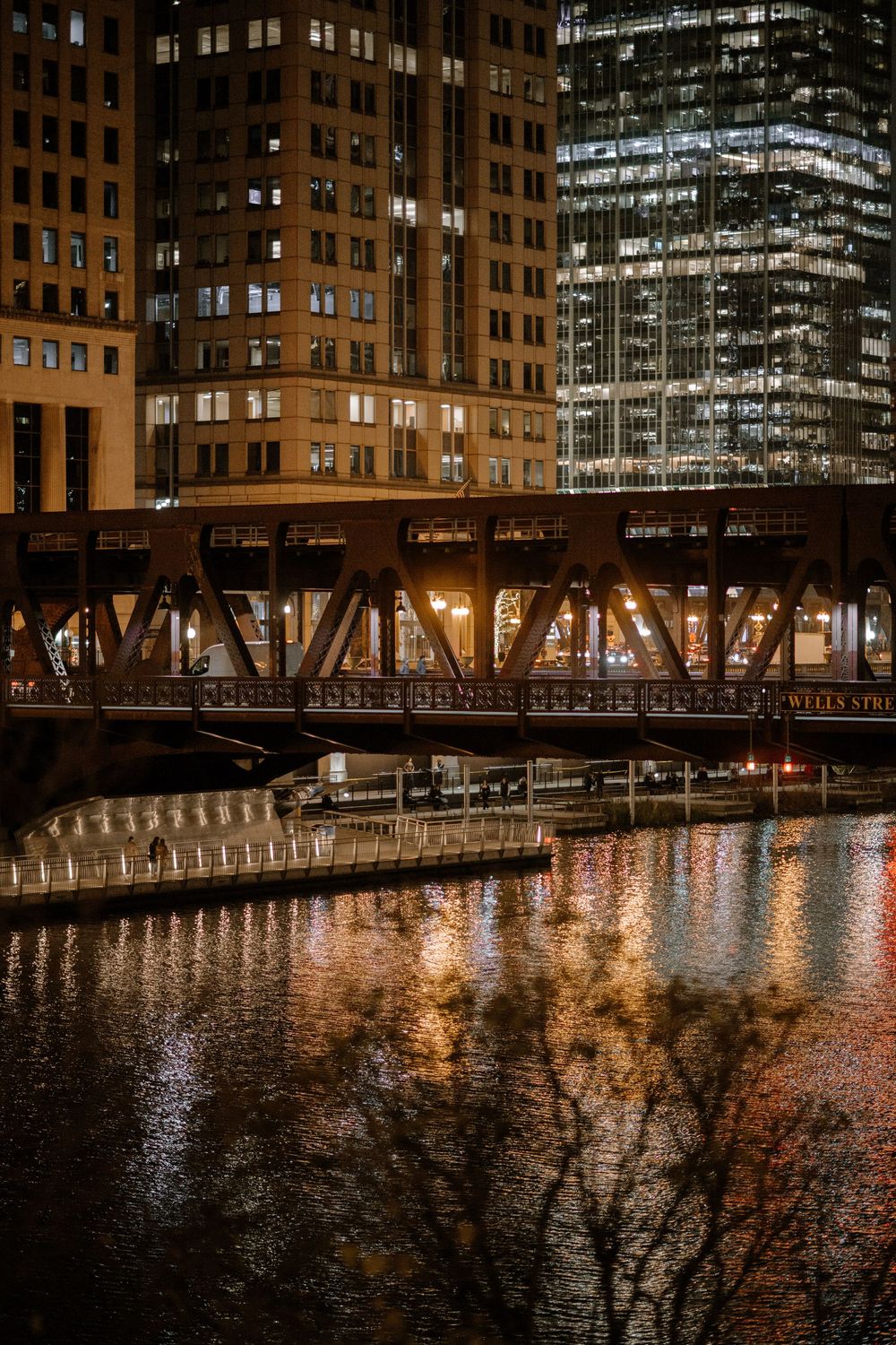 Night view of Chicago River with illuminated Wells Street Bridge and glowing skyscrapers reflecting on water.