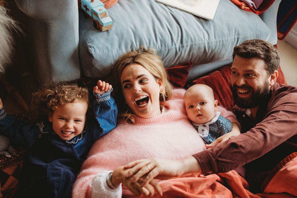 A joyful family moment captured from above as they lay together laughing and cuddling on blue bedding.