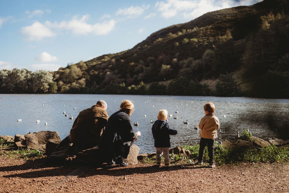 People sit on rocks by a serene lake surrounded by mountains during a peaceful outdoor gathering.