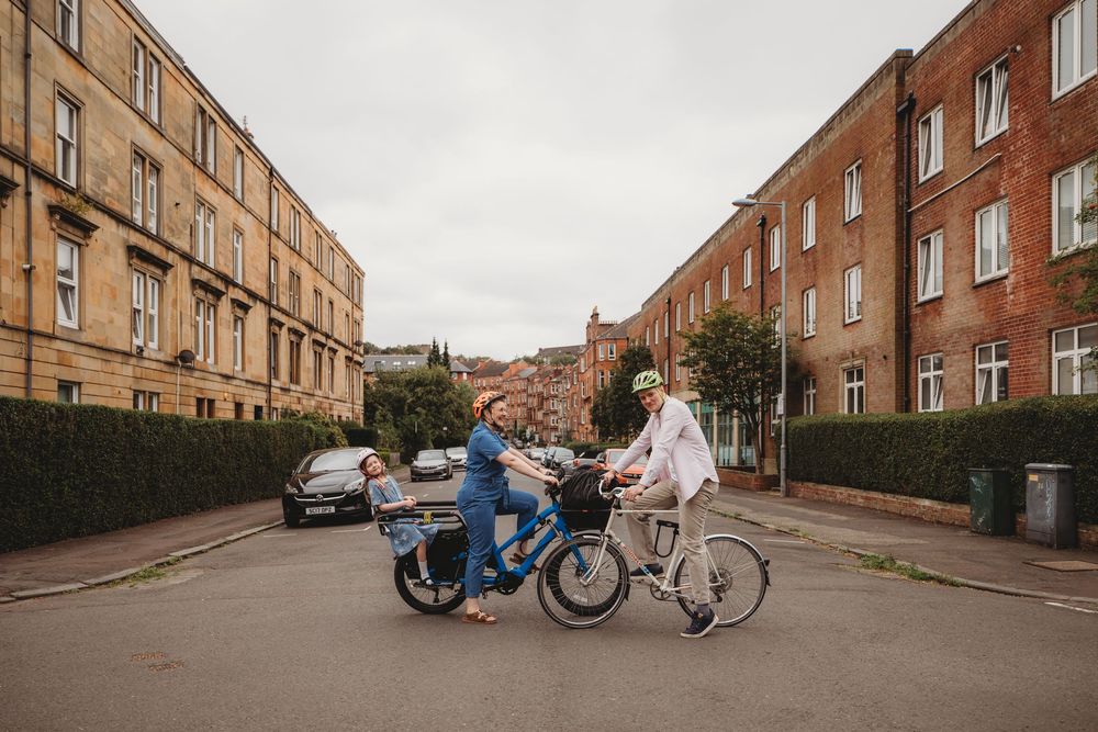 A series of brick apartment buildings line a residential street with bicycles and people visible in the distance.