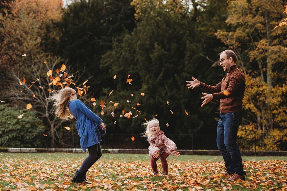 A family plays together tossing fallen autumn leaves in the air during a fun outdoor photoshoot.
