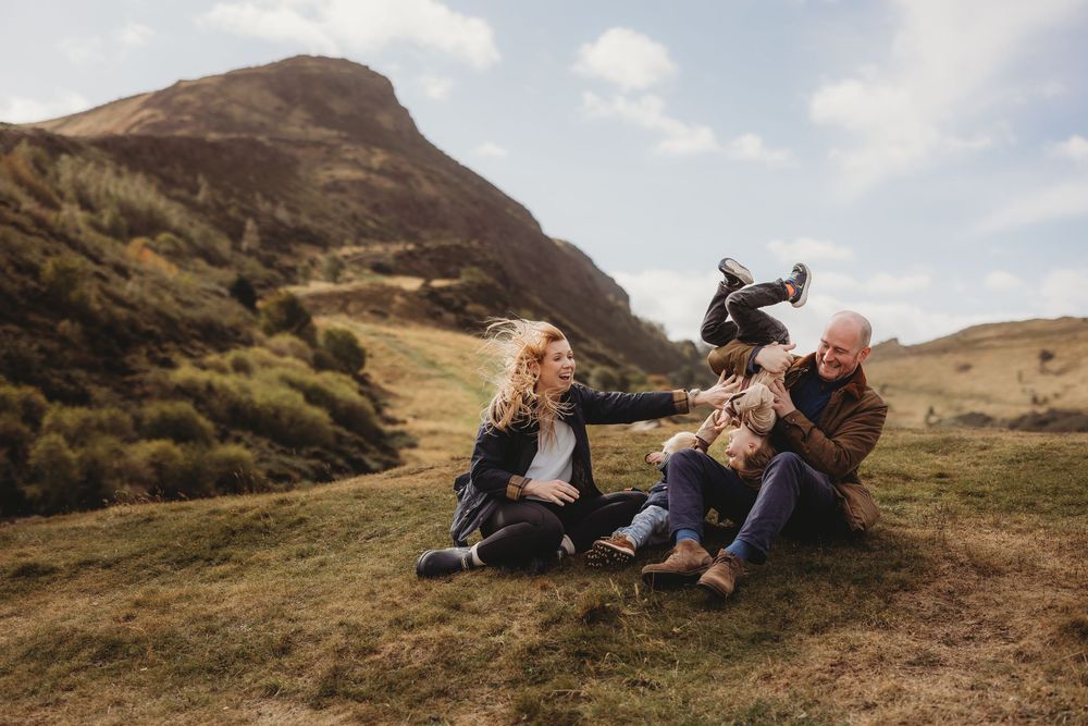 A couple shares an intimate moment together while laying in the grass on a scenic mountainside during sunset.