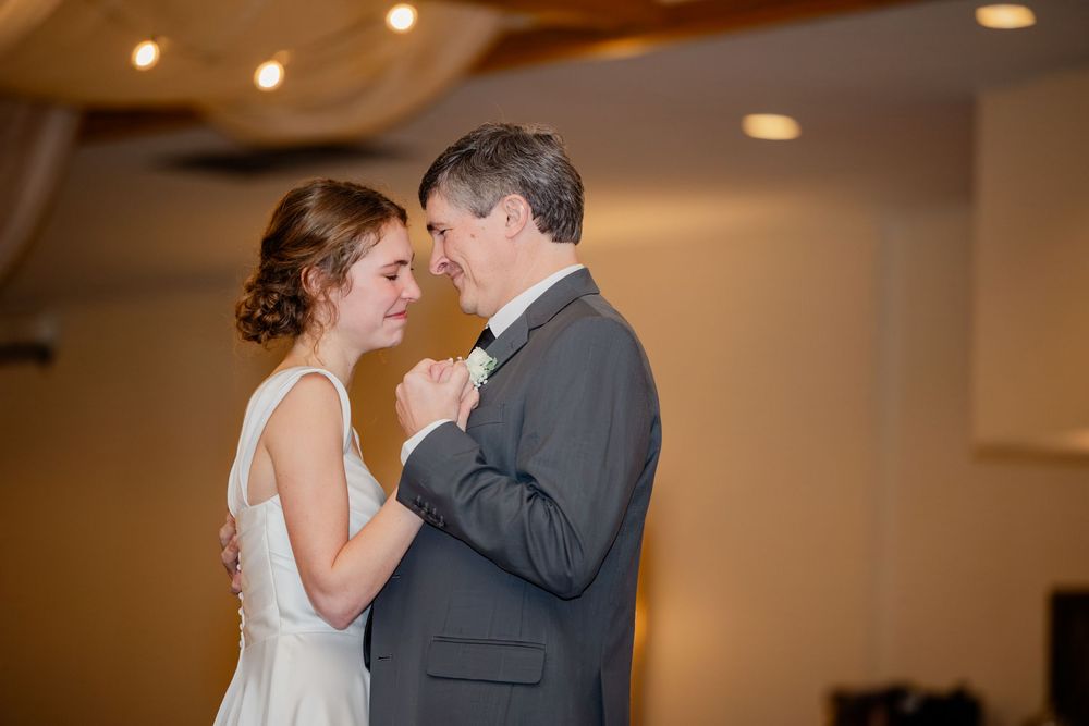 Bride and father share an emotional first dance at wedding reception in elegant venue with warm lighting.