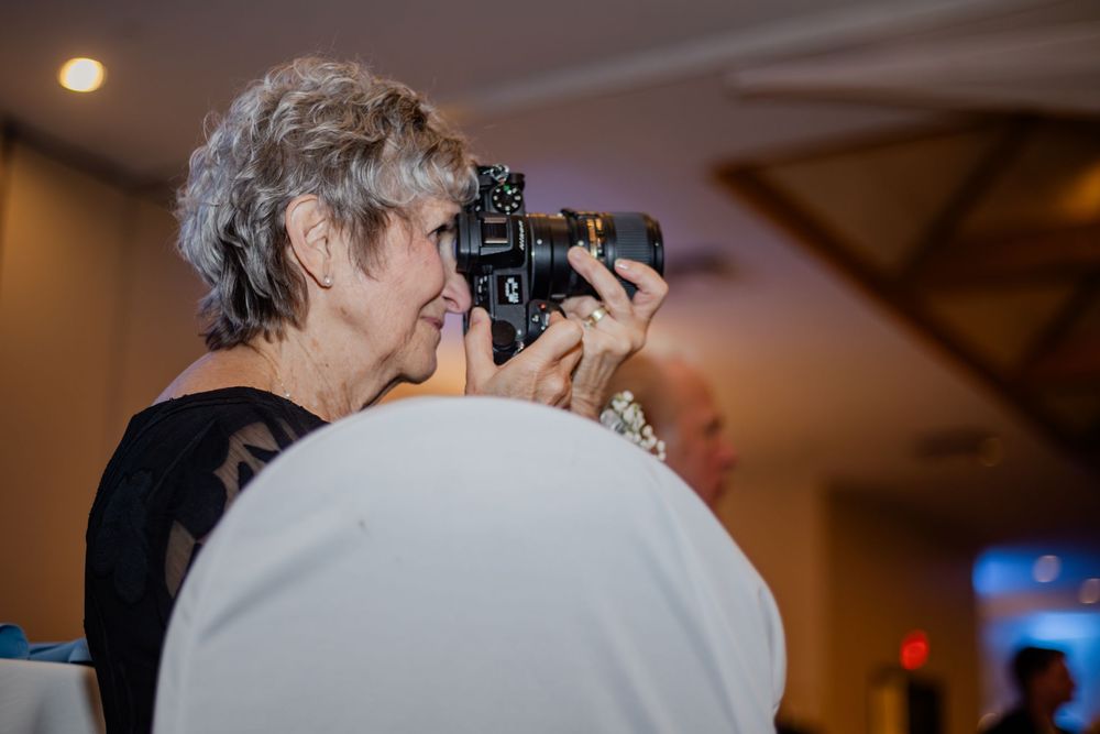Elderly woman with gray hair photographing with a professional camera at an indoor event venue.
