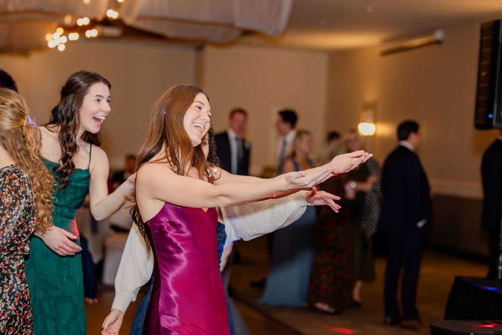 Guests in formal attire dance joyfully at elegant wedding reception with string lights overhead.