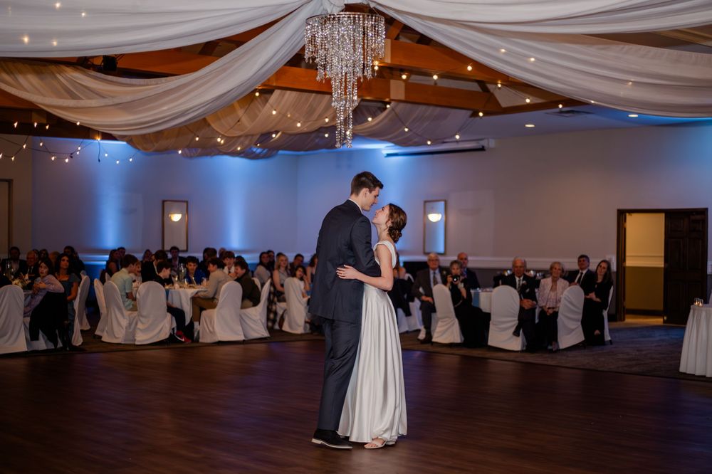 Bride and groom share their first dance in an elegant wedding reception hall with draped ceilings and blue uplighting.