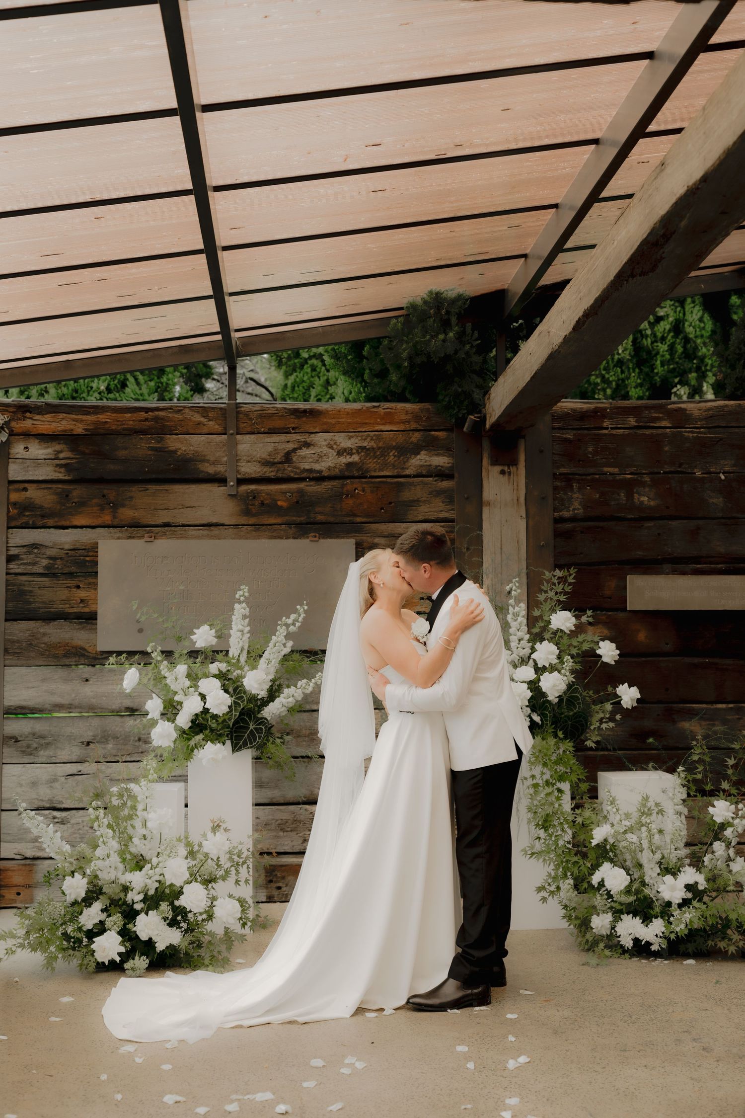 Bride in lace wedding gown with cathedral veil stands on staircase holding a bouquet in a classic home.